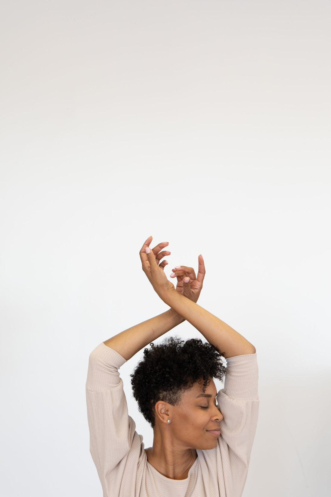A woman in love with herself raises her arms above her head in a soft and happy pose.